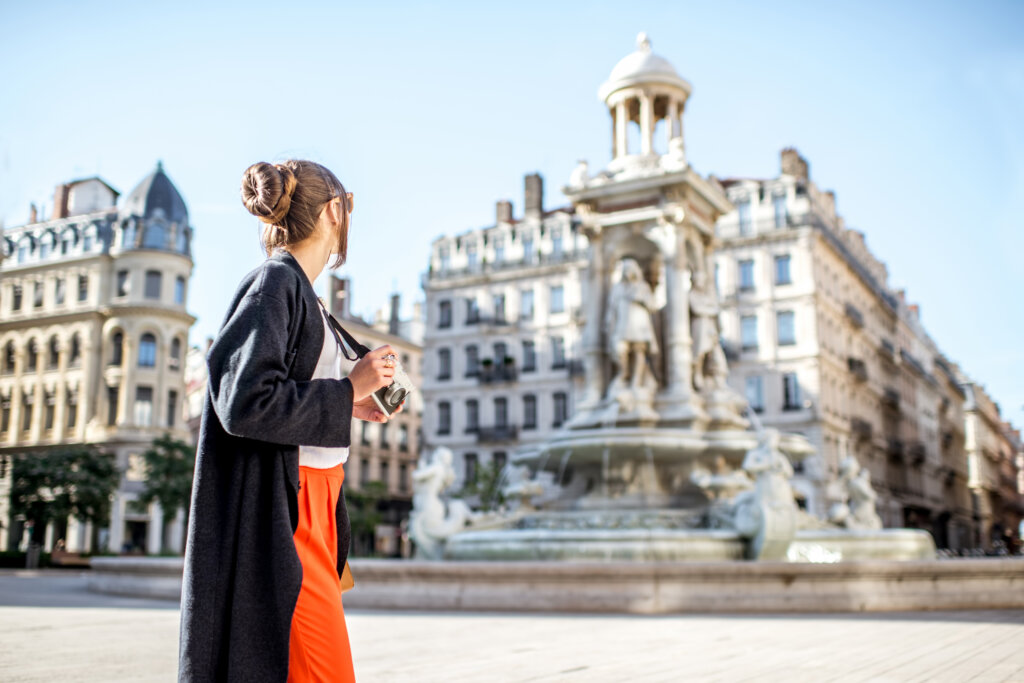 Young woman standing with photo camera on the Jacobins square with famous fountain on the background in Lyon city in France